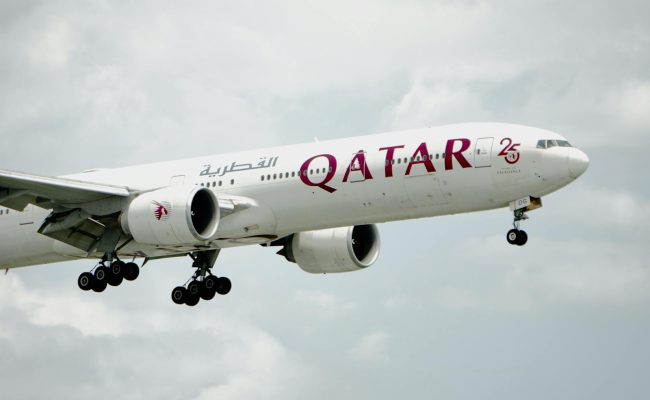 A Qatar Airways plane soaring through cloudy sky, showcasing modern aviation technology.
